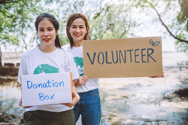 Un groupe de bénévoles tient une pancarte bénévole lors de l'événement de la journée mondiale de l'environnement la conservation des bénévoles ramasse les déchets en plastique et en mousse dans la zone de la forêt de mangroveVolunteering save world concept