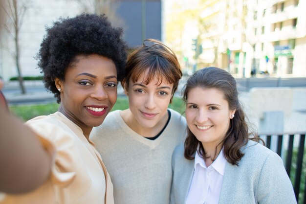 Groupe de femmes gaies prenant selfie sur rue