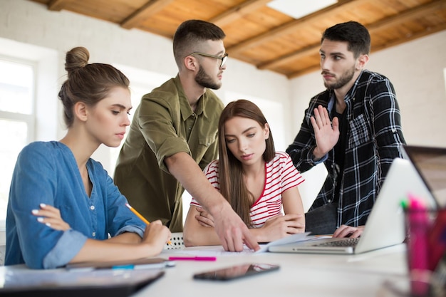 Groupe d'hommes et de femmes d'affaires travaillant pensivement avec des croquis tout en passant du temps au travail Jeunes discutant avec émotion d'un nouveau projet ensemble dans un bureau moderne