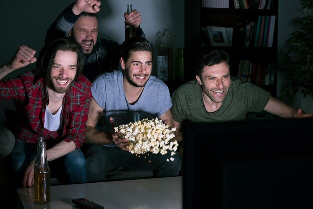 Groupe d'hommes mangeant des pop-corn et regardant le football à la télévision