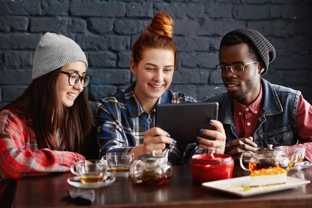 Groupe international de trois amis assis au café et regarder des vidéos en ligne à l'aide d'une tablette