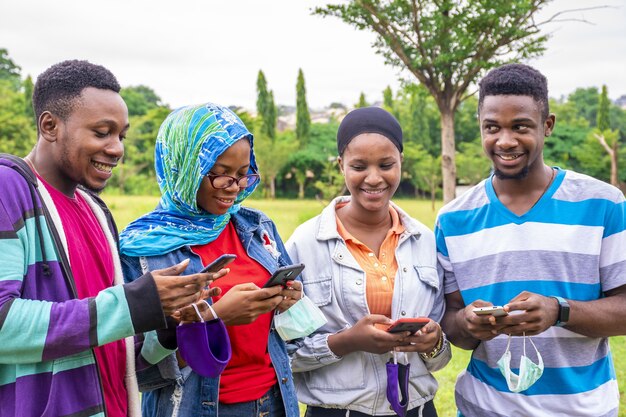 Groupe de jeunes amis africains avec des masques utilisant leur téléphone dans un parc