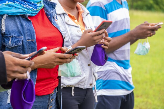 Groupe de jeunes amis africains avec des masques utilisant leur téléphone dans un parc