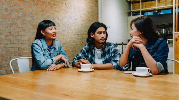 Groupe de jeunes amis asiatiques heureux s'amusant et riant en savourant un repas assis ensemble au café-restaurant.