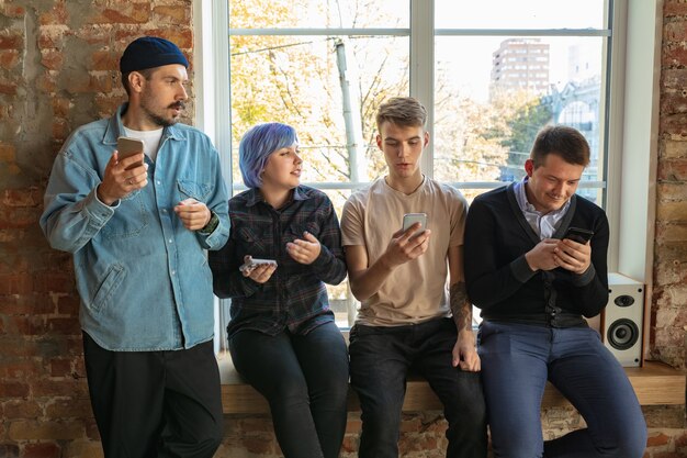 Groupe de jeunes caucasiens heureux debout derrière la fenêtre. Partager une actualité, des photos ou des vidéos depuis des smartphones, parler ou jouer à des jeux et s'amuser. Médias sociaux, technologies modernes.