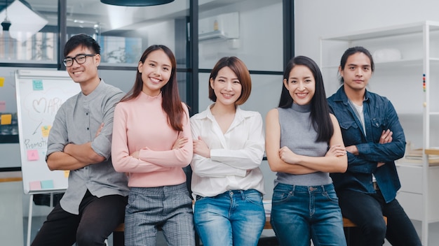 Groupe de jeunes créatifs asiatiques en vêtements décontractés intelligents souriants et bras croisés sur un lieu de travail de bureau créatif.