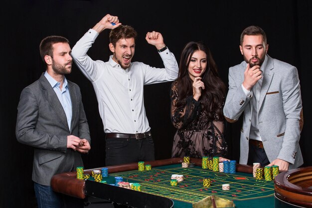 Groupe de jeunes derrière la table de roulette sur fond noir. Le jeune homme se réjouit de la victoire