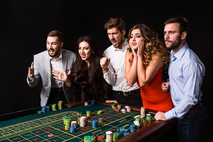Photo gratuit groupe de jeunes derrière la table de roulette sur fond noir. les jeunes ont fait des paris dans le jeu et attendent le résultat. émotions vives