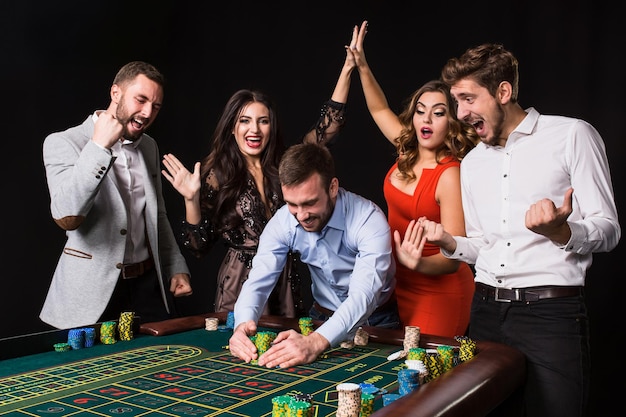 Groupe de jeunes derrière la table de roulette sur fond noir. Joueur gagnant. Émotions vives