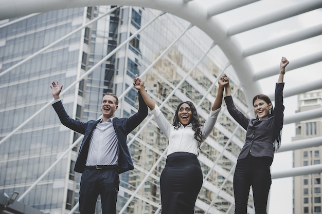 Photo gratuite groupe de jeunes entrepreneurs heureux avec les mains dans les airs succès sur leurs plans.