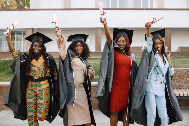 Groupe de jeunes étudiantes afro-américaines vêtues d'une robe de graduation noire. Le campus en arrière-plan