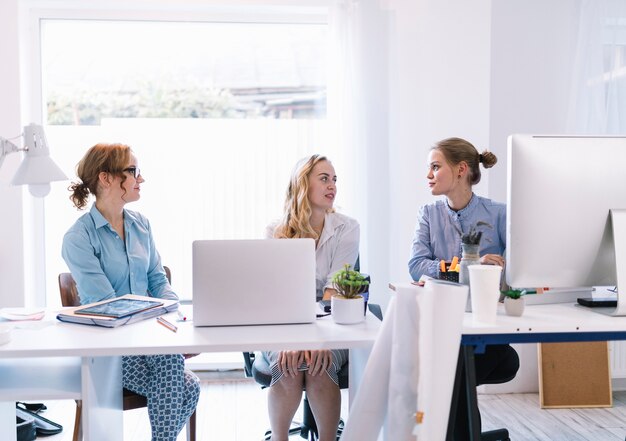 Groupe de jeunes femmes d&#39;affaires assis dans un bureau moderne se parlant