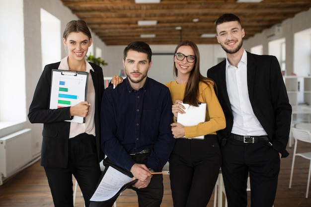 Groupe de jeunes hommes d'affaires souriants en costumes classiques regardant joyeusement à huis clos tout en passant du temps au travail dans un bureau moderne