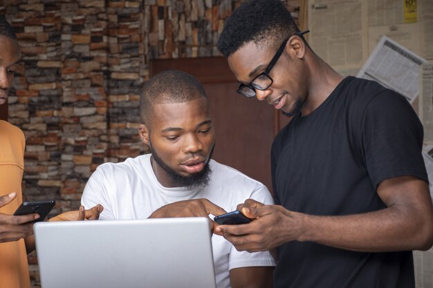 Groupe de jeunes hommes africains discutant d'un projet tout en utilisant leur ordinateur portable et leurs téléphones