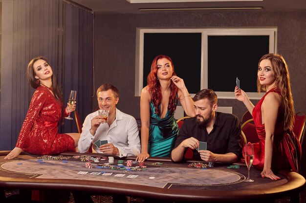 Un groupe de jeunes joueurs pose à une table de poker dans un casino et regarde la caméra. Les jeunes font des paris en attendant une grande victoire. Jouer pour de l'argent. Jeux de fortune.