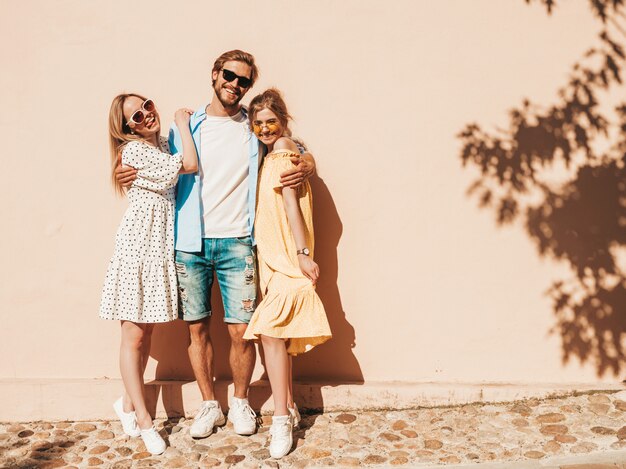 Groupe de jeunes trois amis élégants posant dans la rue. Homme de mode et deux jolies filles vêtues de vêtements d'été décontractés. Sourire, modèles, amusant, lunettes soleil., Gai, femmes, et, type, devenir fou