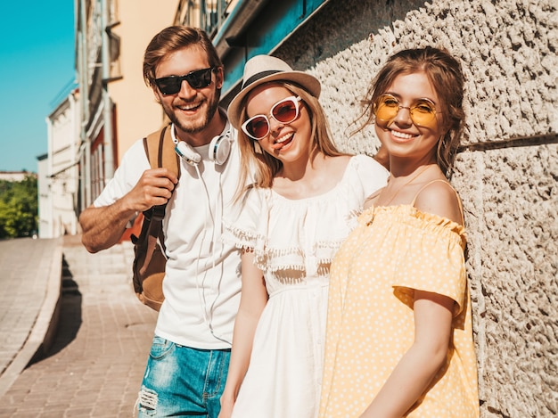 Groupe de jeunes trois amis élégants posant dans la rue. Homme de mode et deux jolies filles vêtues de vêtements d'été décontractés. Sourire, modèles, amusant, lunettes soleil., Gai, femmes, et, type, montrer, langue