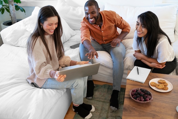 Photo gratuite groupe de jeunes utilisant un ordinateur portable ensemble à la maison sur un canapé et prenant des collations