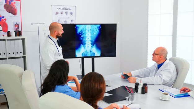 Groupe de médecins écoutant un expert médical lors d'une conférence médicale analysant la radiographie numérique, pointant sur le moniteur. Médecins utilisant la technologie moderne discutant du diagnostic sur le traitement des patients