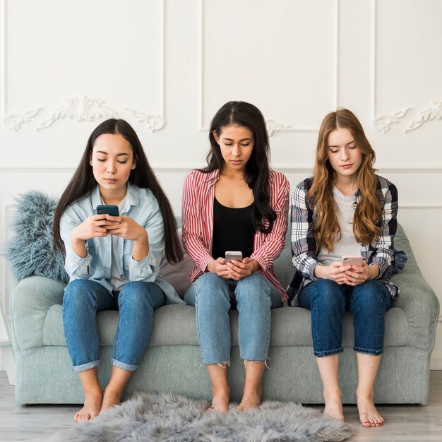 Groupe multiethnique d&#39;adolescents assis à l&#39;aide de téléphones