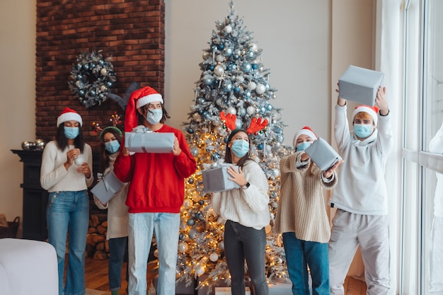 Groupe multiethnique d'amis en chapeaux de Père Noël avec des cadeaux en mains.