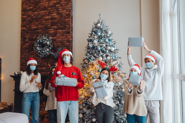 Groupe multiethnique d'amis en chapeaux de Père Noël souriant et posant avec des cadeaux en mains