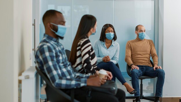 Groupe multiethnique de candidats recevant des papiers d'emploi, se préparant à commencer un entretien d'embauche avec le service des ressources humaines. Les gens attendent dans le hall pour assister à une réunion pendant la pandémie.