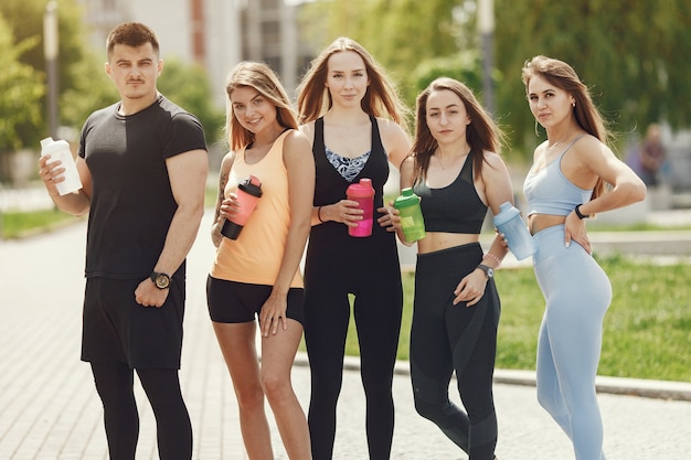 Groupe de personnes dans un parc. Garçon avec quatre filles. Les sportifs avec des bouteilles d'eau.