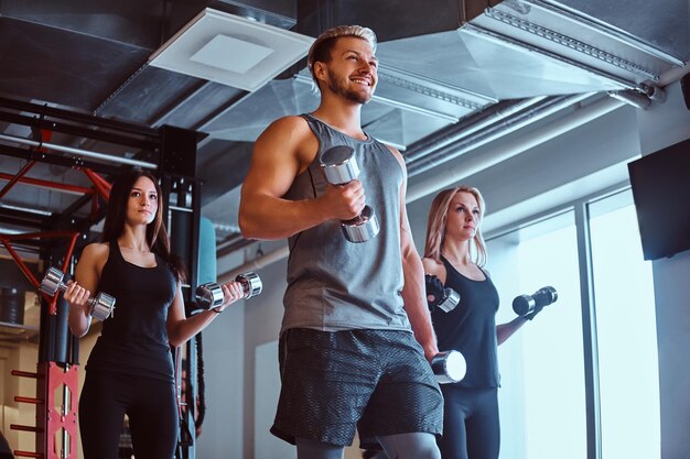 Groupe de personnes faisant de l'exercice avec des haltères dans le club de fitness ou la salle de sport.