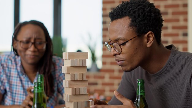 Groupe de personnes joyeuses s'amusant avec une tour en bois, jouant à des jeux de société avec des blocs carrés et des pièces de construction. Heureux amis jouant avec des cubes pour les loisirs.