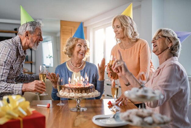 Groupe de personnes matures célébrant l'anniversaire de la femme et s'amusant à la fête à la maison