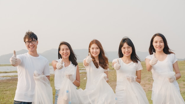 Un groupe de portraits de jeunes volontaires multiethniques aide à garder la nature propre en regardant devant et en souriant avec des sacs poubelles blancs sur la plage