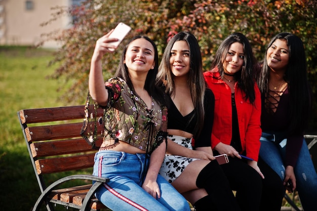 Groupe de quatre filles latinos heureuses et jolies de l'Équateur posées dans la rue et faisant un selfie au téléphone