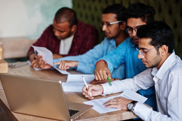 Groupe de quatre hommes sud-asiatiques posés lors d'une réunion d'affaires dans un café Indiens ensemble et signent des documents importants Contrat pour étudier et travailler