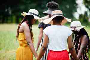 Photo gratuite groupe de quatre magnifiques femmes afro-américaines portant un chapeau d'été se tenant la main et priant à l'herbe verte dans le parc