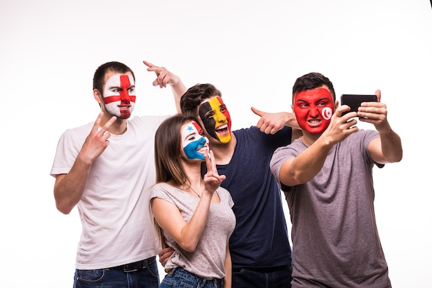 Photo gratuite un groupe de supporters soutient leurs équipes nationales avec des visages peints. angleterre, belgique, tunisie, panama fans prennent selfie sur téléphone isolé sur fond blanc