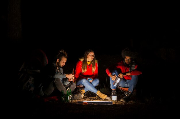 Groupe de trois amis campant dans la forêt avec lumière LED la nuit