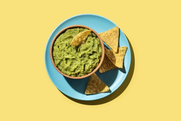 Guacamole mexicain avec chips nacho dans un bol en bois sur fond jaunexA