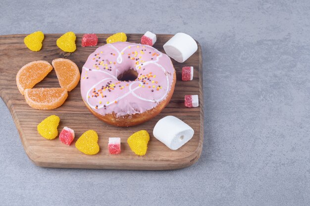 Guimauves, marmelades et un beignet sur une planche de bois sur une surface en marbre