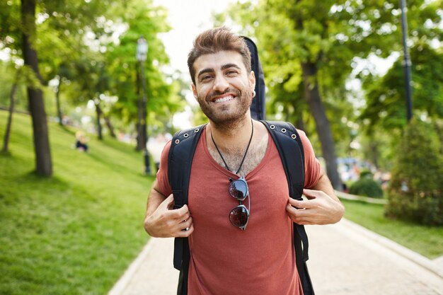 Guitariste souriant insouciant, gars avec guitare marchant dans le parc heureux