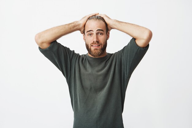 Guy attrayant barbu tenant la tête avec les mains ayant une expression de maladresse