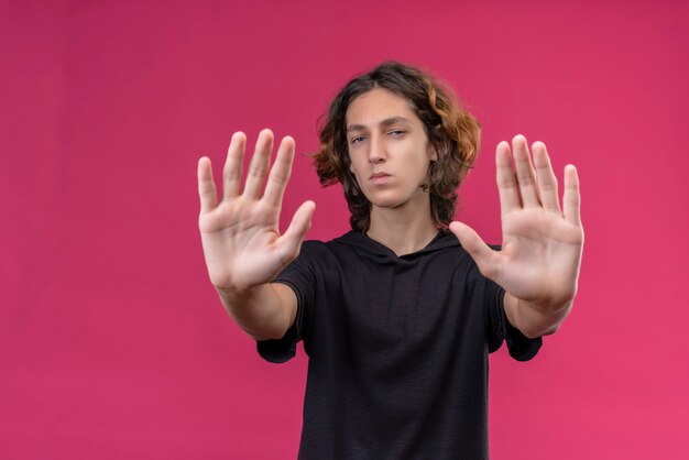 Guy aux cheveux longs en t-shirt noir montrant cinq avec ses deux mains sur le mur rose