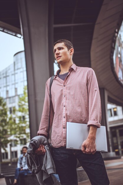 Guy dans la rue moderne en vêtements décontractés avec ordinateur portable