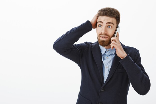 Guy debout stupéfait recevant une offre géniale. Portrait de surpris et heureux entrepreneur mâle caucasien sans voix en costume formel élégant toucher coupe de cheveux parler via téléphone portable étonné