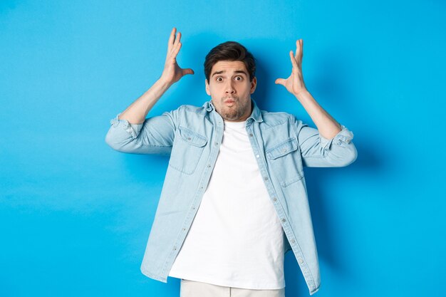 Guy en détresse montrant un geste époustouflant, l'air frustré et anxieux, debout sur fond bleu