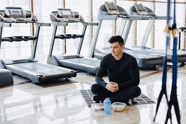 Guy élégant dans la salle de gym se détendre sur le sol et manger des aliments sains.