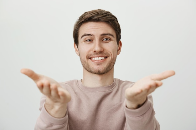 Guy est très heureux de vous voir. Charmant frère caucasien sympathique dirigeant avec des paumes et regardant avec une expression heureuse et satisfaite