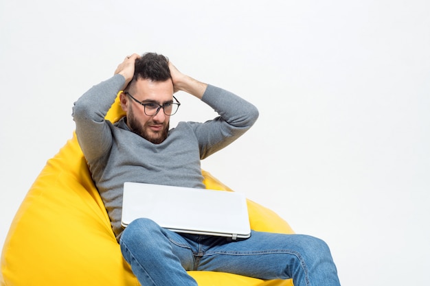 Photo gratuite guy frustré alors qu'il était assis sur une chaise pouf jaune