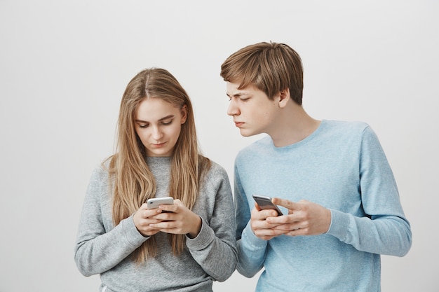 Guy furtivement au téléphone des filles avec un visage sérieux. Messagerie des frères et sœurs sur smartphone