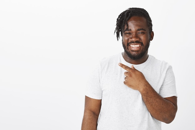 Guy joyeux insouciant avec des tresses posant contre le mur blanc